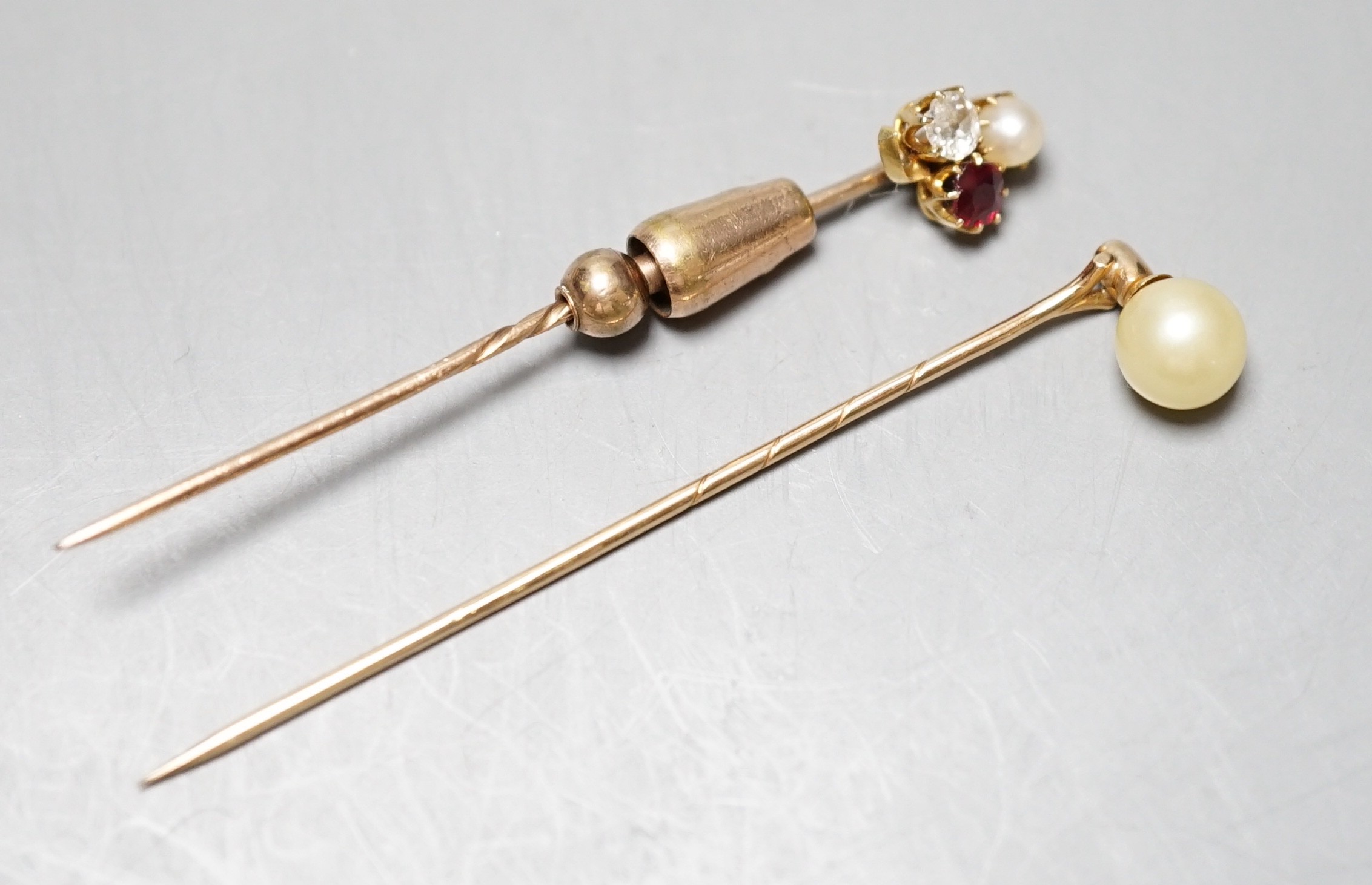An early 20th century yellow metal, ruby, diamond and cultured pearl cluster set stick pin, 58mm and a yellow metal and simulated pearl stick pin.